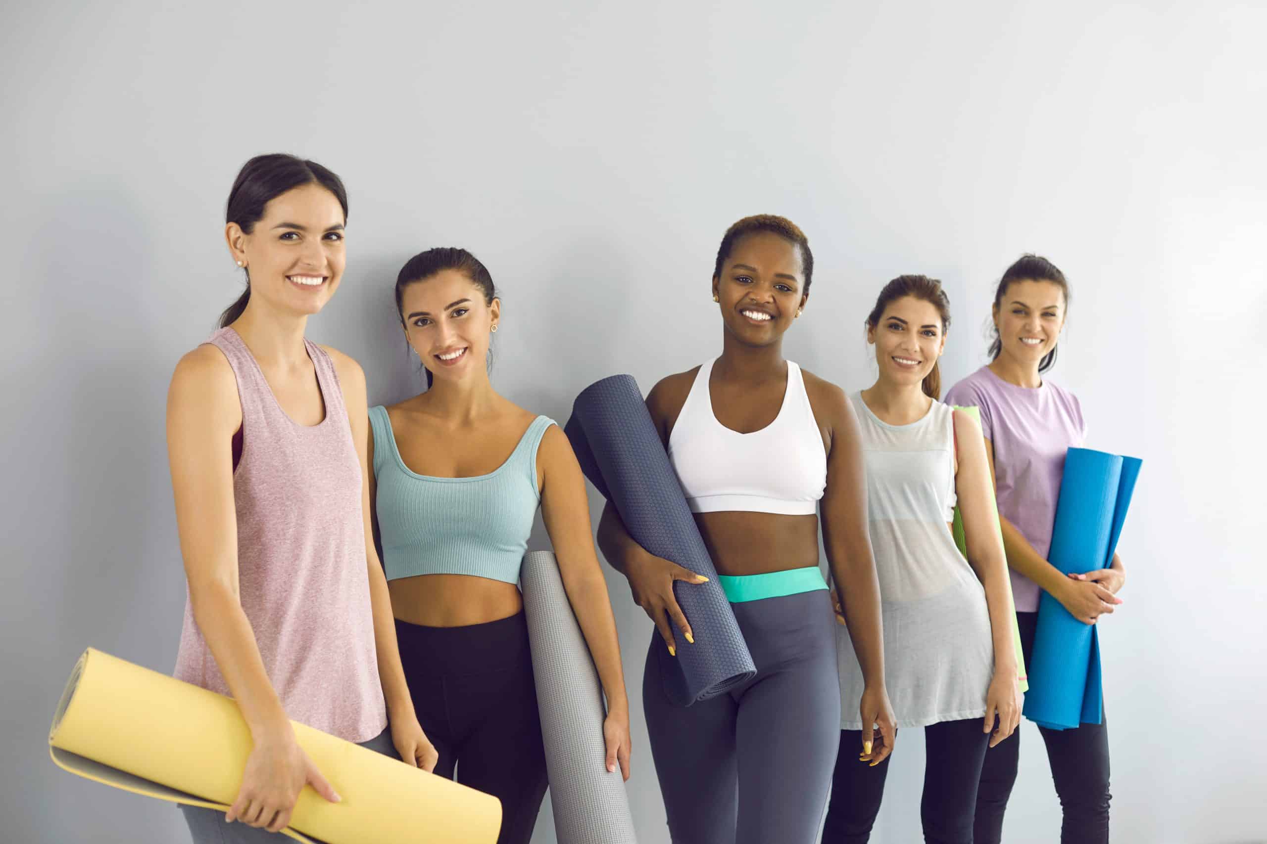 Group portrait of happy young women in activewear holding workout mats and smiling